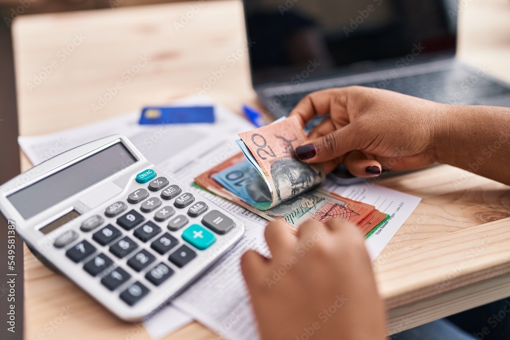 African american woman ecommerce business worker using calculator counting australian dollars at office African american woman ecommerce business worker using calculator counting australian dollars at office