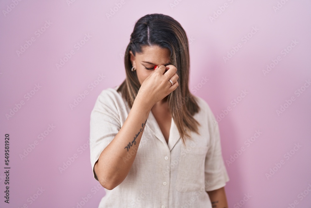 Blonde woman standing over pink background tired rubbing nose and eyes feeling fatigue and headache. stress and frustration concept. Blonde woman standing over pink background tired rubbing nose and eyes feeling fatigue and headache. stress and frustration concept.