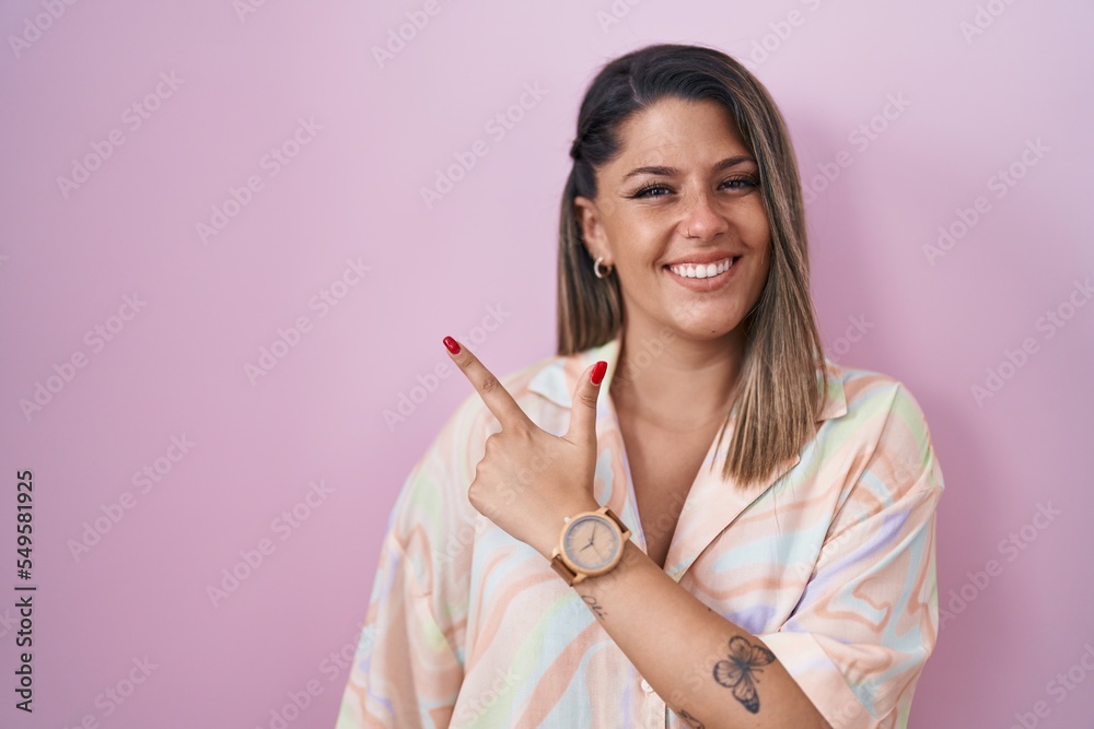 Blonde woman standing over pink background cheerful with a smile of face pointing with hand and finger up to the side with happy and natural expression on face Blonde woman standing over pink background cheerful with a smile of face pointing with hand and finger up to the side with happy and natural expression on face