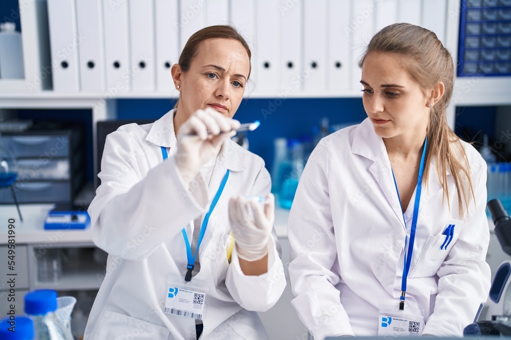 Two women scientists using laptop holding pill at laboratory