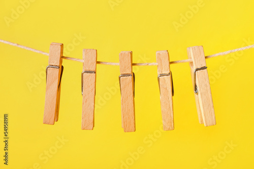 Wooden clothespins hanging on rope against yellow background