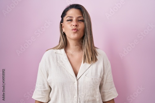 Blonde woman standing over pink background looking at the camera blowing a kiss on air being lovely and sexy. love expression.