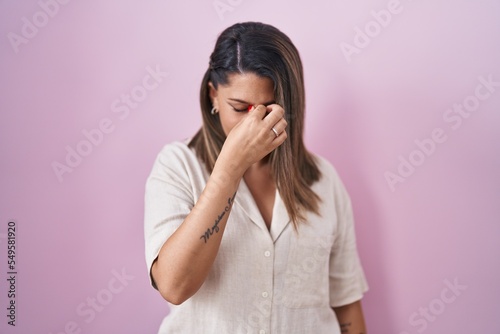 Blonde woman standing over pink background tired rubbing nose and eyes feeling fatigue and headache. stress and frustration concept.