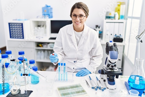 Young hispanic woman wearing scientist uniform using pipette at laboratory