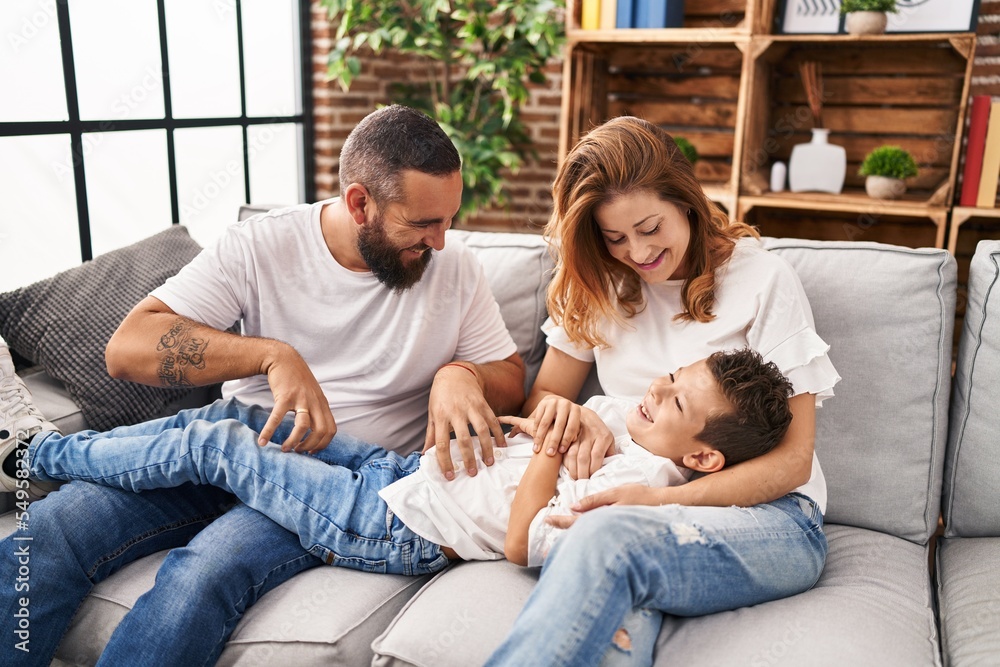 Family doing tickle to son sitting on sofa at home Family doing tickle to son sitting on sofa at home
