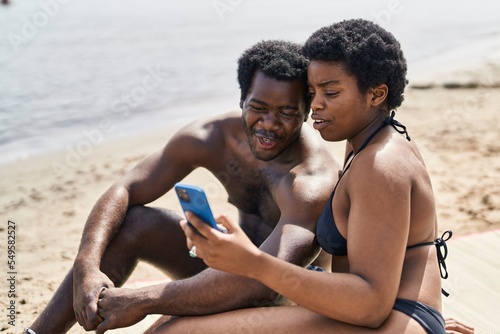 African american man and woman couple wearing swimsuit using smartphone at seaside