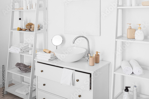 Sink and shelf units with bath accessories near white wall © Pixel-Shot
