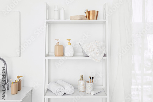 Shelf unit with bath accessories near white wall in bathroom © Pixel-Shot