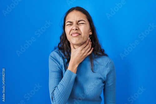 Young brazilian woman standing over blue isolated background touching painful neck, sore throat for flu, clod and infection