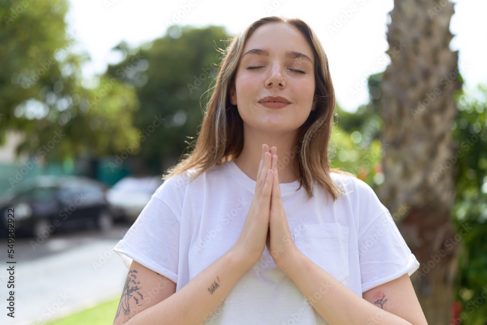 Naklejka premium Young caucasian woman doing yoga exercise at park