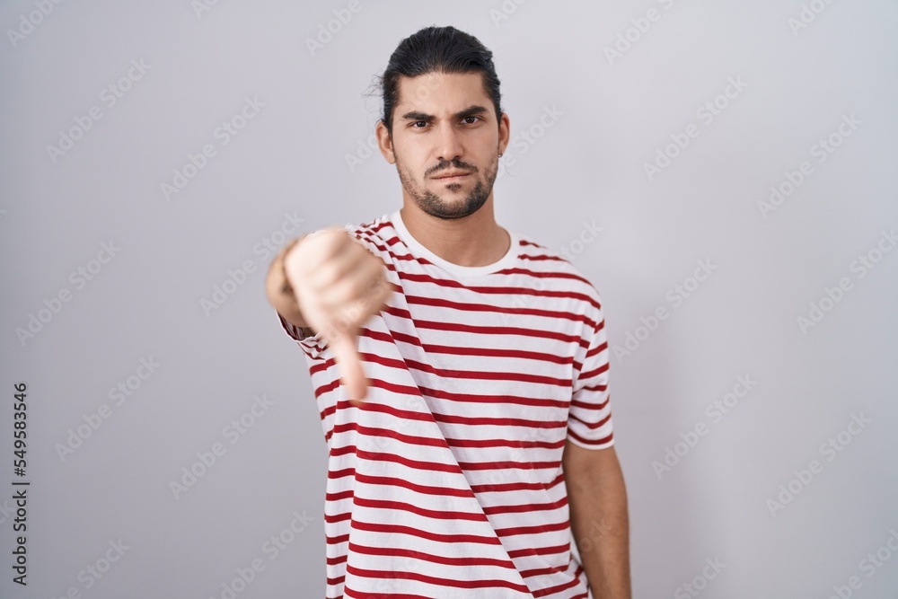 Fototapeta premium Hispanic man with long hair standing over isolated background looking unhappy and angry showing rejection and negative with thumbs down gesture. bad expression.