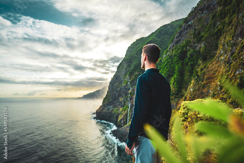 Man in shirt looking at waterfall flowing into the sea in atmospheric morning atmosphere. Viewpoint Véu da Noiva, Madeira Island, Portugal, Europe. photo