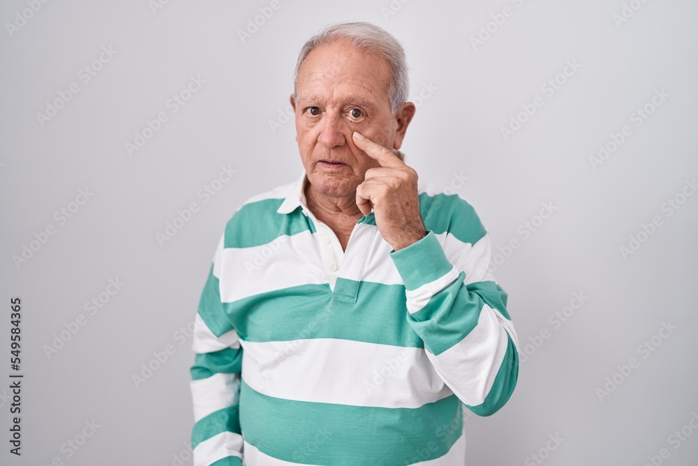 Senior man with grey hair standing over white background pointing to the eye watching you gesture, suspicious expression Senior man with grey hair standing over white background pointing to the eye watching you gesture, suspicious expression