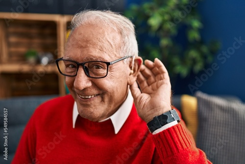 Senior man smiling confident using deafness hearing aid at home