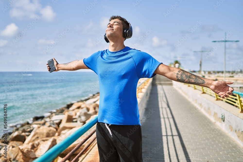 Young latin man breathing using headphones and smartphone at the beach. Young latin man breathing using headphones and smartphone at the beach.