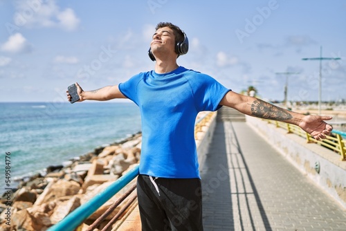 Young latin man breathing using headphones and smartphone at the beach.