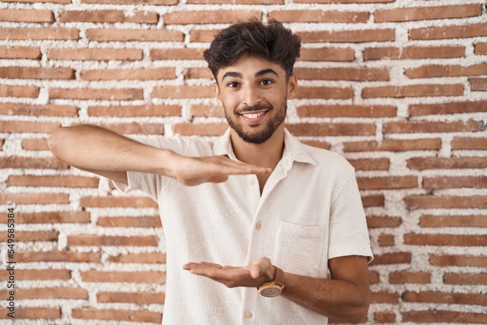 Arab man with beard standing over bricks wall background gesturing with hands showing big and large size sign, measure symbol. smiling looking at the camera. measuring concept. Arab man with beard standing over bricks wall background gesturing with hands showing big and large size sign, measure symbol. smiling looking at the camera. measuring concept.