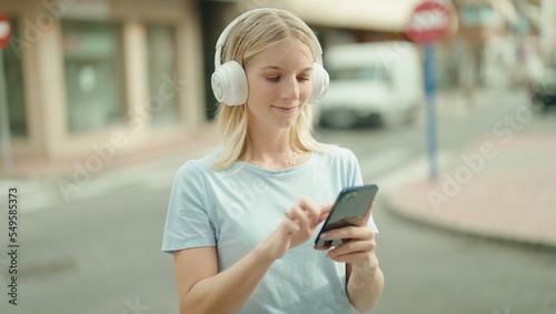 Young blonde woman listening to music standing at street