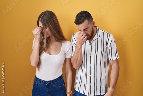 Young couple standing over yellow background tired rubbing nose and eyes feeling fatigue and headache. stress and frustration concept.