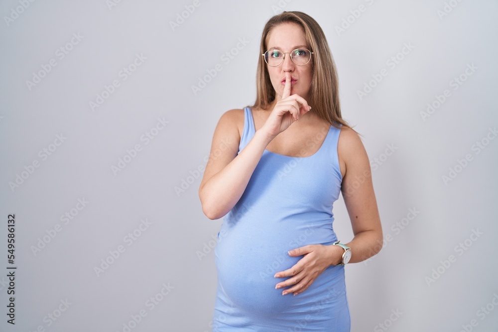 Young pregnant woman standing over white background asking to be quiet with finger on lips. silence and secret concept. Young pregnant woman standing over white background asking to be quiet with finger on lips. silence and secret concept.