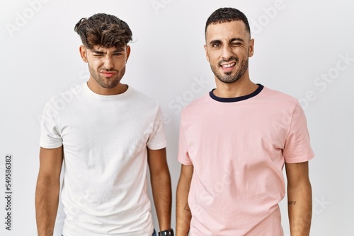 Young gay couple standing over isolated background winking looking at the camera with sexy expression, cheerful and happy face.