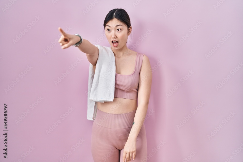 Chinese young woman wearing sportswear and towel pointing with finger surprised ahead, open mouth amazed expression, something on the front Chinese young woman wearing sportswear and towel pointing with finger surprised ahead, open mouth amazed expression, something on the front