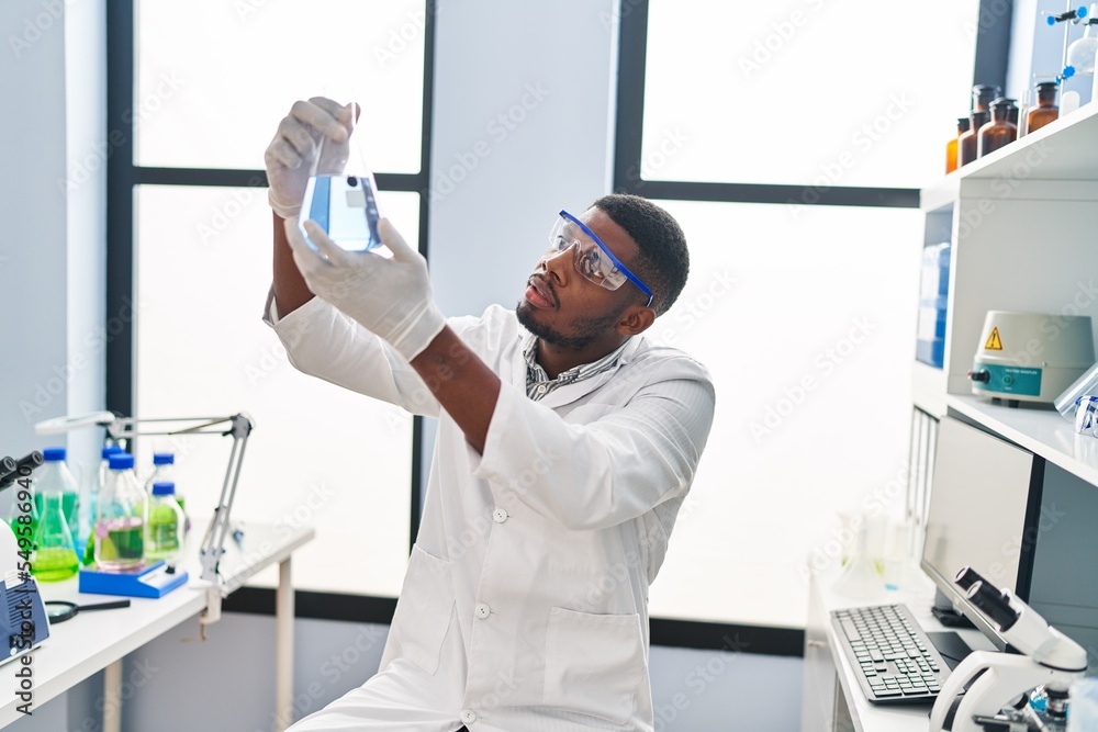 Young african american man wearing scientist uniform holding test tube at laboratory Young african american man wearing scientist uniform holding test tube at laboratory