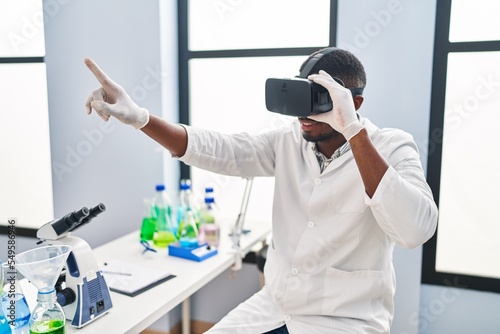 Young african american man wearing scientist uniform using virtual reality glasses at laboratory