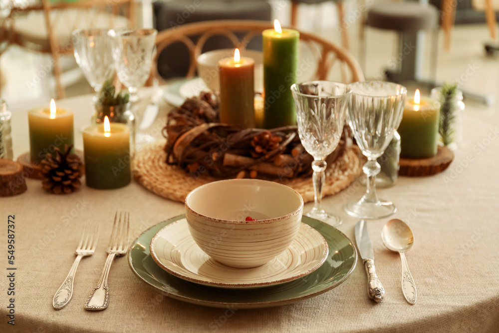 Christmas table setting with burning candles and wreath in kitchen, closeup