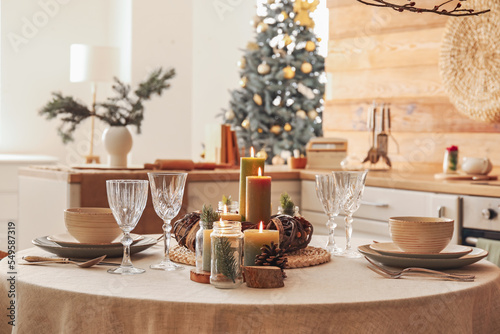 Christmas table setting with burning candles and wreath in kitchen