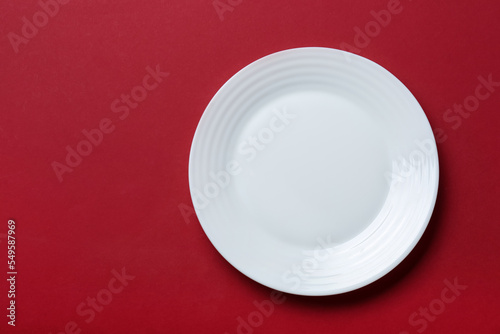 Empty white ceramic plate on red background, top view. Space for text