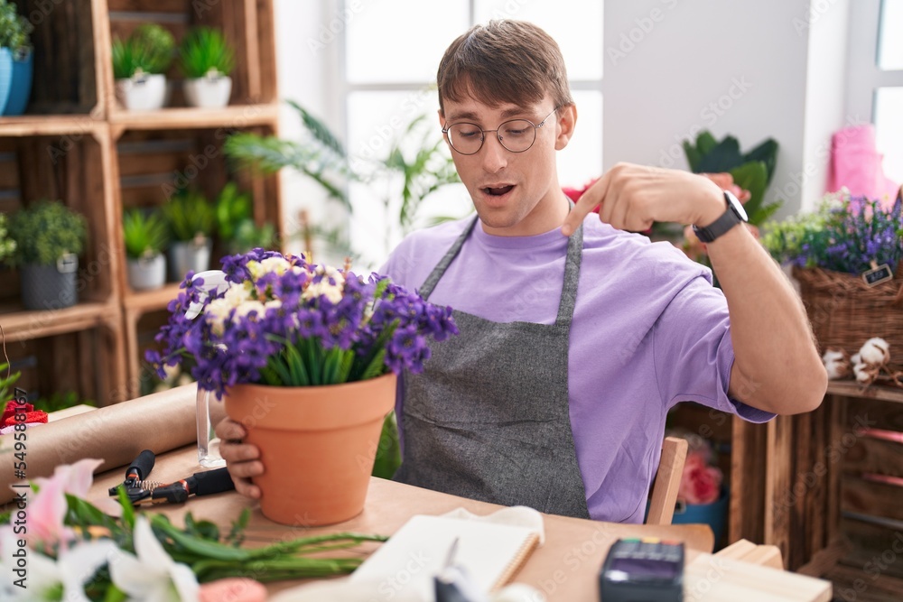 Caucasian blond man working at florist shop pointing down with fingers showing advertisement, surprised face and open mouth
