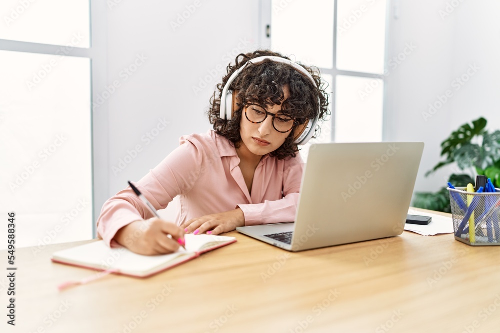 Young middle east businesswoman using headphones and laptop writing on diary working at the office. Young middle east businesswoman using headphones and laptop writing on diary working at the office.
