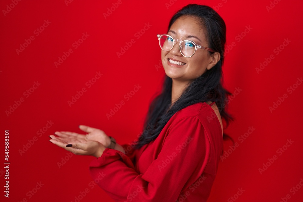 Asian young woman standing over red background pointing aside with hands open palms showing copy space, presenting advertisement smiling excited happy Asian young woman standing over red background pointing aside with hands open palms showing copy space, presenting advertisement smiling excited happy
