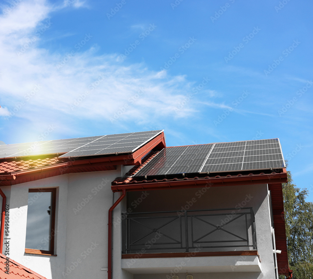 House with installed solar panels on roof under blue sky. Alternative energy source House with installed solar panels on roof under blue sky. Alternative energy source