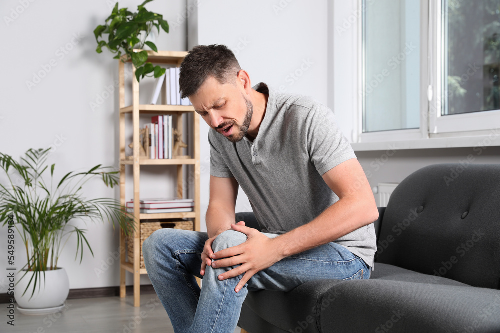 Man suffering from knee pain on sofa at home