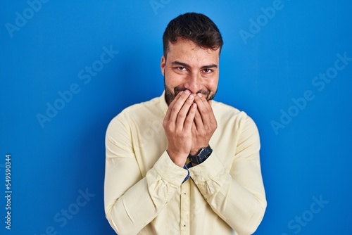 Fotografie Handsome hispanic man standing over blue background laughing and embarrassed gig
