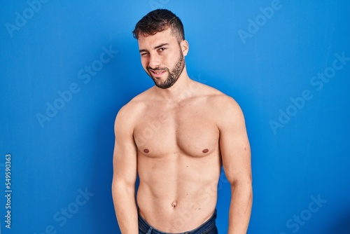 Handsome hispanic man standing shirtless winking looking at the camera with sexy expression, cheerful and happy face.
