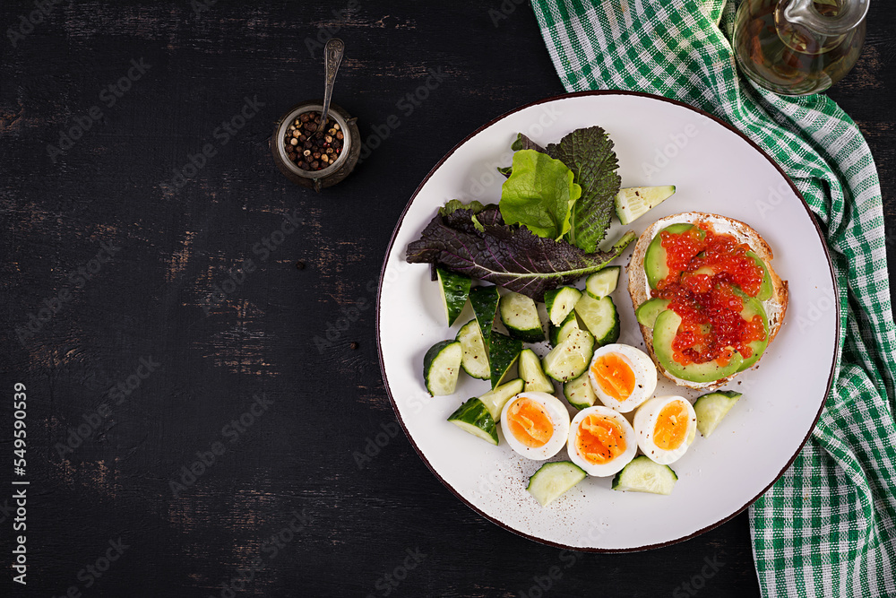 Breakfast. Healthy open sandwich on  toast with avocado and red caviar, boiled eggs, cucumber salad on white plate. Healthy protein food. Top view