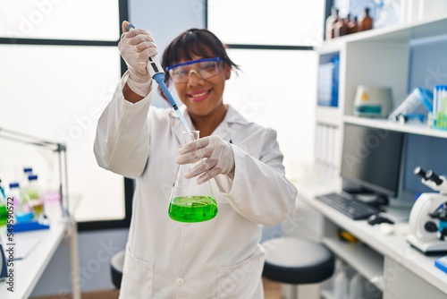 Young beautiful latin woman scientist smiling confident pouring liquid on test tube at laboratory