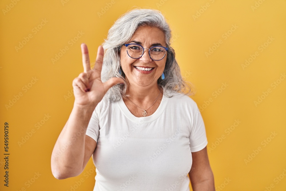 Middle age woman with grey hair standing over yellow background showing and pointing up with fingers number three while smiling confident and happy. Middle age woman with grey hair standing over yellow background showing and pointing up with fingers number three while smiling confident and happy.