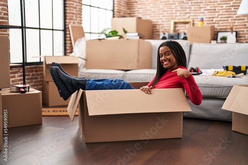 Young african american with braids moving to a new home inside of a cardboard box pointing finger to one self smiling happy and proud © Krakenimages.com