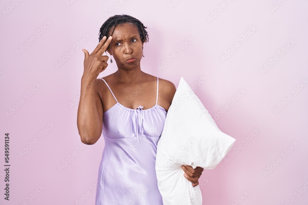 African woman with dreadlocks wearing pajama hugging pillow shooting and killing oneself pointing hand and fingers to head like gun, suicide gesture. African woman with dreadlocks wearing pajama hugging pillow shooting and killing oneself pointing hand and fingers to head like gun, suicide gesture.