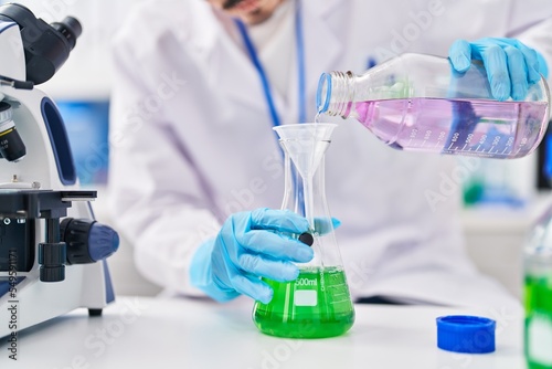 Young caucasian man scientist pouring liquid on test tube at laboratory