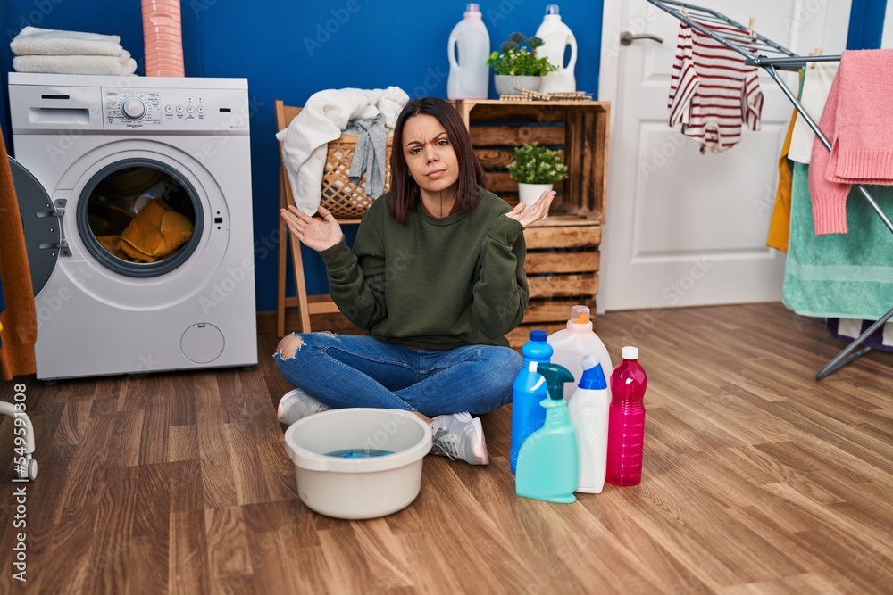 Young hispanic woman doing laundry washing by hand clueless and confused expression with arms and hands raised. doubt concept. Young hispanic woman doing laundry washing by hand clueless and confused expression with arms and hands raised. doubt concept.