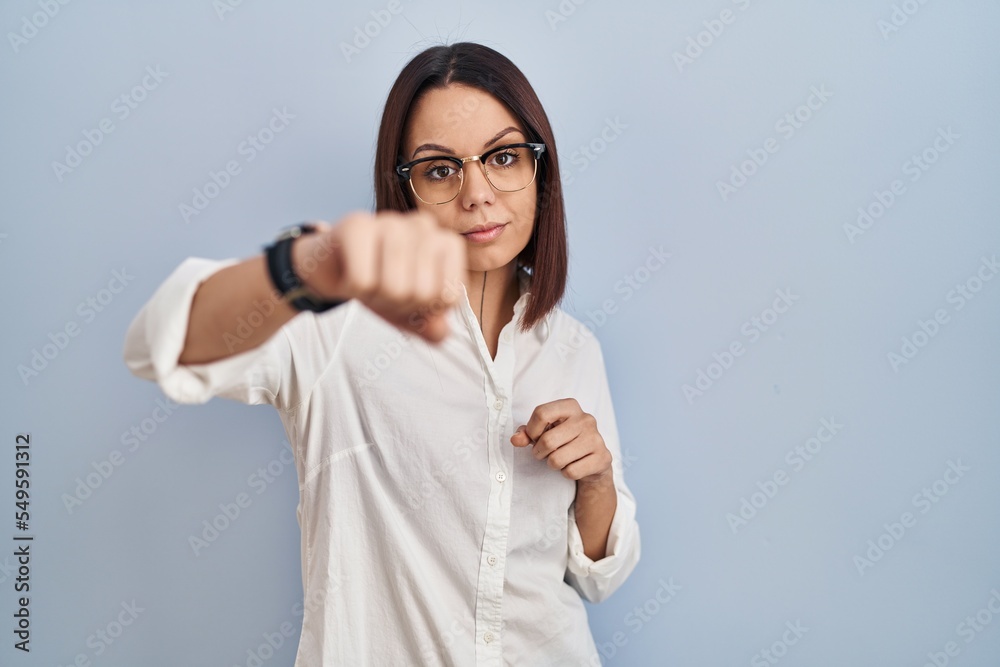 Young hispanic woman standing over white background punching fist to fight, aggressive and angry attack, threat and violence Young hispanic woman standing over white background punching fist to fight, aggressive and angry attack, threat and violence