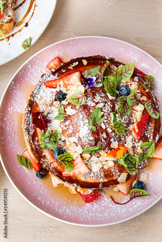 Top view of plate of Freshly homemade waffles with ice cream, caramel sauce and fresh berries on top of waffles on wooden desk