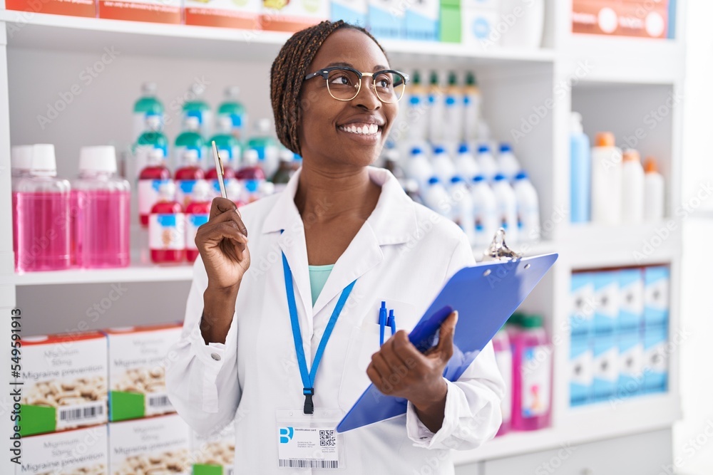 African american woman pharmacist smiling confident holding clipboard at pharmacy