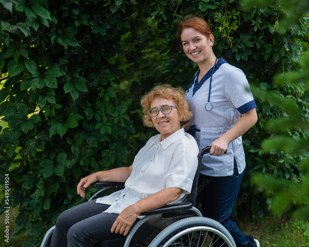 Caucasian female doctor walks with an elderly patient in a wheelchair in the park. Nurse accompanies an old woman on a walk outdoors. Caucasian female doctor walks with an elderly patient in a wheelchair in the park. Nurse accompanies an old woman on a walk outdoors.
