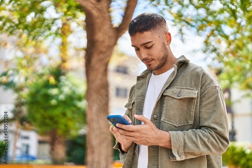 Tableau sur toile Young hispanic man smiling confident using smartphone at park